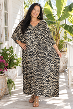 Load image into Gallery viewer, A woman modeling a leopard-print kaftan dress on a sunlit porch with potted plants and white house siding in the background.