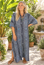 Load image into Gallery viewer, A woman modeling a loose, knee-length kaftan dress with a black, white, and blue geometric pattern in an outdoor garden courtyard setting.