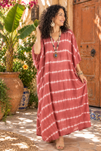 Load image into Gallery viewer, A woman wearing a loose, long-sleeve tie-dye kaftan dress in dusty rose and white, standing in a sunlit courtyard with a wooden door, potted plants, and stone flooring.